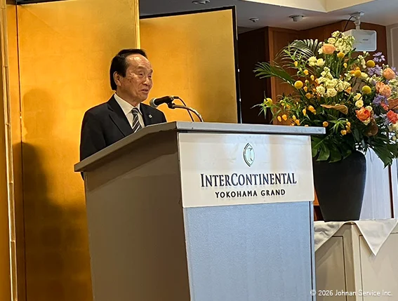 演台に立ち挨拶を行う社長。背後には金屏風と花が飾られている。