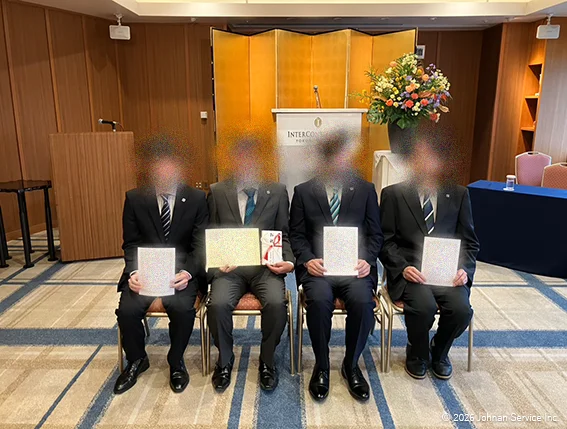 昇進者と永年勤続表彰者あわせて4名の社員が、辞令または表彰状を手に着席し記念撮影を行っている様子。