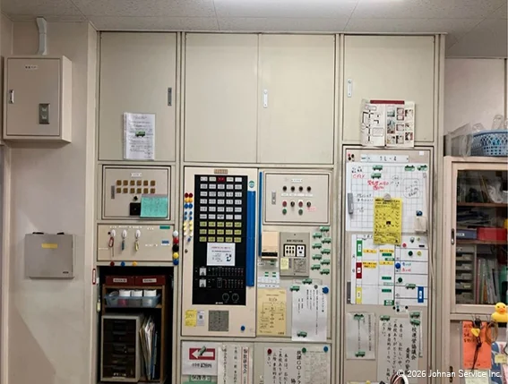 改修前の総合盤。操作ボタンや表示器、連絡用の掲示物が並び、既設設備が使用されている状態。