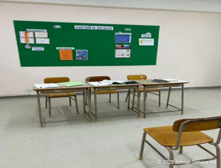 面接準備のために机と椅子が並べられている様子。机の上にはノートや書類が広げられ、背景には緑色の掲示板に案内やポスターが貼られている。