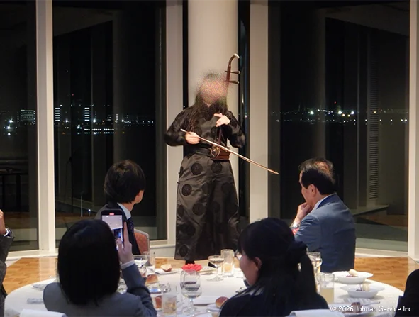 演奏者が二胡を弾いている様子。前方を囲む参加者たちが着席し演奏に注目している様子。